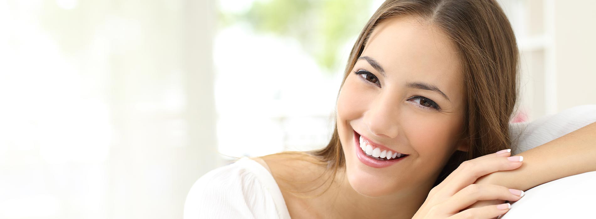 The image shows a woman with a radiant smile looking directly at the camera, her eyes closed, with her hand resting on her face. She appears to be in a serene environment, possibly a room with soft lighting.