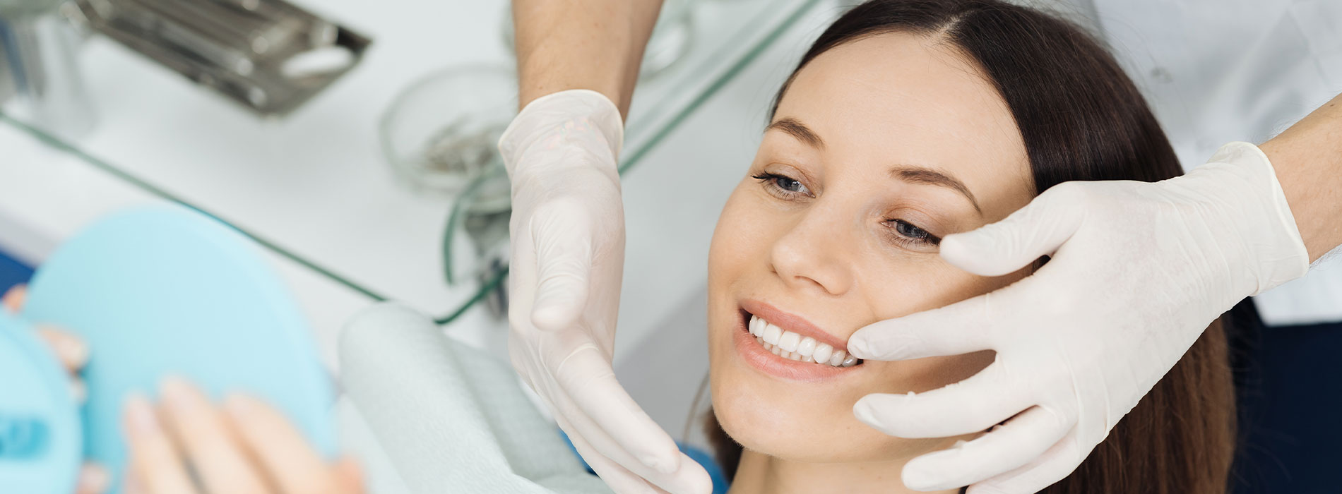 A woman receiving a facial treatment with a visible blue mask on her face, being attended to by a professional wearing white gloves and a surgical mask, set against a blurred background of a medical environment.