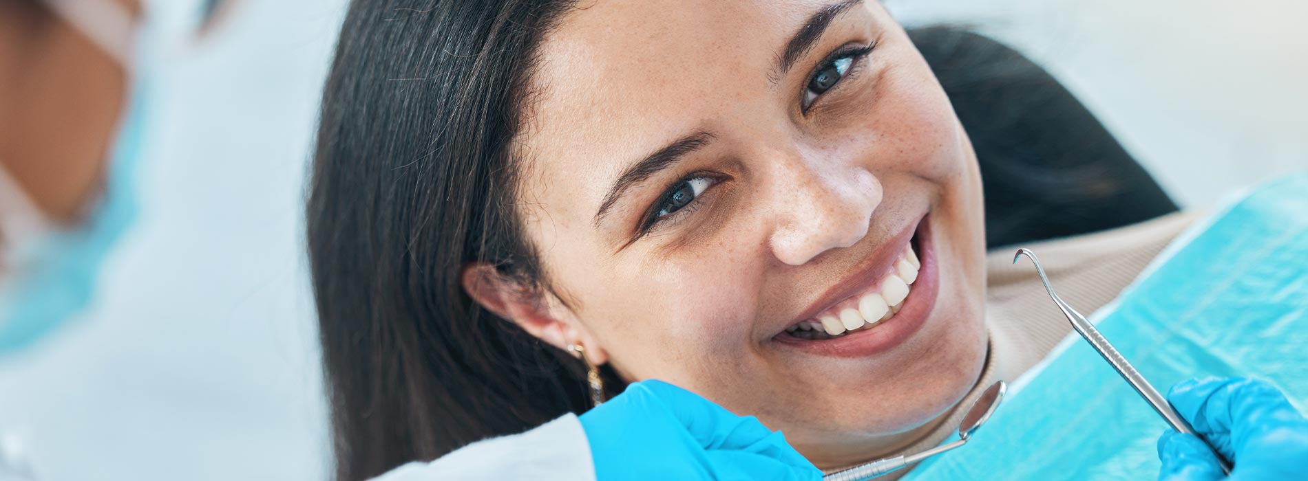 The image features a smiling woman with dark hair, wearing a blue surgical mask, sitting in front of a group of people who appear to be medical professionals, with one person holding a stethoscope around their neck.