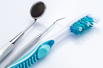 The image shows a collection of dental instruments on a white background, including a toothbrush with blue bristles.