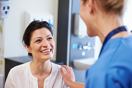 The image shows two individuals in a medical setting  one appears to be a patient receiving care from a healthcare professional, with both smiling at each other.