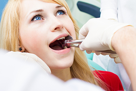 The image shows a woman receiving dental care with a dental professional performing an oral examination using a dental mirror and light.