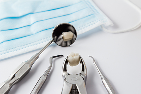 The image shows a dental tool with a tooth filling in place, placed on a blue cloth, surrounded by other dental instruments, including tweezers and scissors, all set against a white background.