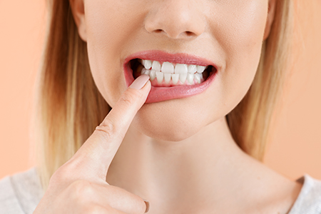 The image shows a woman with her finger on her teeth, holding a toothpaste tube, against a bright background.