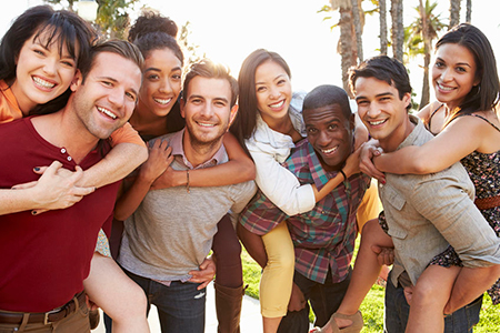 A group of young adults posing together outdoors during the daytime, smiling and hugging each other for a photo.