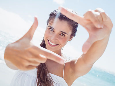 The image shows a woman with her hand outstretched, appearing to be taking a selfie with a camera, against a bright background.